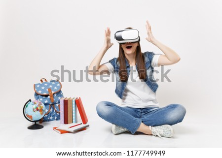 Young amazed woman student wearing virtual reality glasses spreading hands enjoying sitting near globe, backpack, school books isolated on white background. Education in school university college