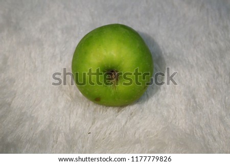 Close-up picture of a green apple on a white fur carpet
