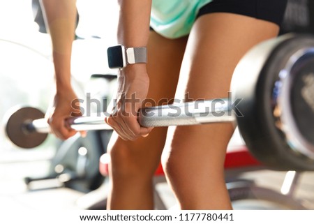 Cropped image of young sports woman doing exercise with barbell in gym
