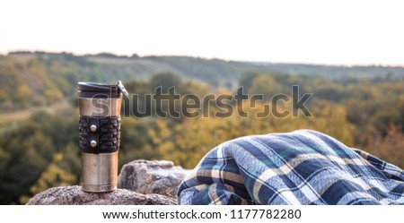 camping items, thermos with jacket on a stone on the background of nature, the concept of travel and recreation