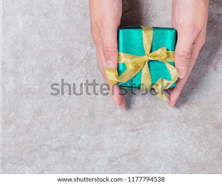 top view hand holding gift box wrapped with gold ribbon on gray background