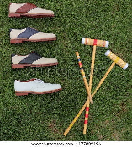 Four leather men's saddle shoes, laying in the grass with croquet mallets for a dressy, luxurious product picture.