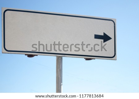 Road sign with directional arrow against the blue cloudless sky. Blank white background, copyspace.