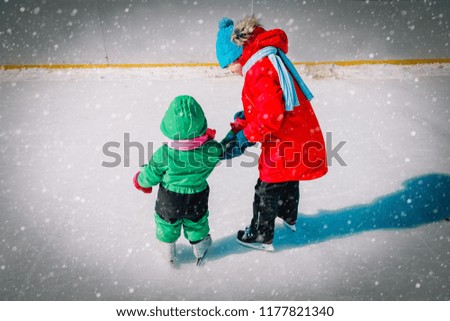 brother teaching little sister to skate in winter