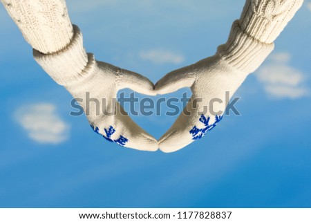 Female hands in the winter mittens in the shape of a heart against a clear blue sky. Concept