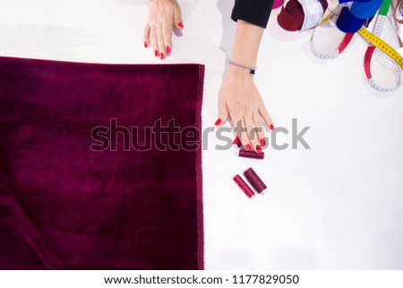 Women's hands and cloths, red cloth lies on the table, hand reaches for the threads