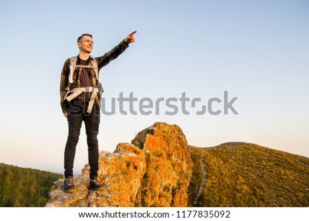 Young traveler stands on a stone and points the finger   the background of the mountains.