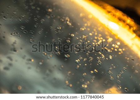 rain drops on the windshield of a car reflects the sky and the sunset