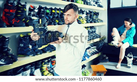 Young sporty guy looking for modern ski boots in sport goods store