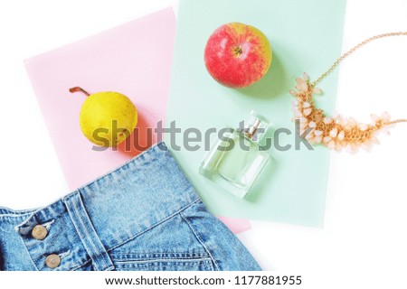 Flat lay fashion and beauty photo. Blue denim skirt, necklace, fresh fruit perfume and yellow pear and red apple. Top view female things