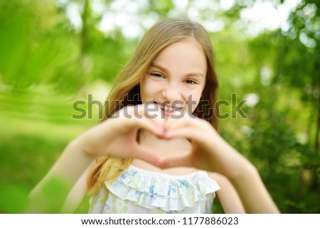 Cute preteen girl laughing and holding her hands in a heart shape on bright and sunny summer day. Cute child enjoying herself outdoors. Happy childhood.