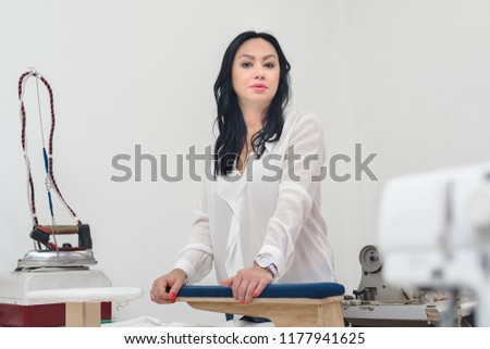 Portrait of pretty female tailor posing with her modern equipment