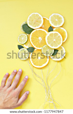 Close-up - A young man's hand holds strings at the end of which citrus fruits such as orange, lemon and lime float away as balloons - concept with citrus fruits as balloons