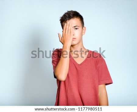 young man closes his eyes with his hands, on the subject of optics or surprise, isolated studio photo on the background