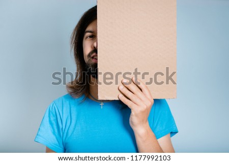 handsome man hiding behind a cardboard, isolated studio photo on a background