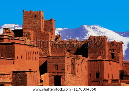Fortified city (ksar and kasbah) of Aït Benhaddou (Ait Ben-Haddou) made of red clay where many foreign films have been shot, with the High Atlas mountains covered by snow in blue sky, Morocco  