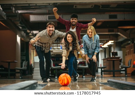 Young woman throwing a bowling ball. Her friends cheering in the back.