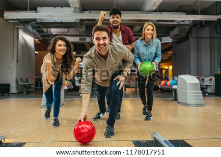 Shot of a handsome young man throwing the bowling ball while his friends are cheering