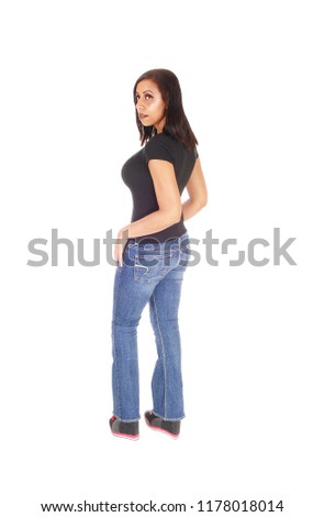 Pretty young woman standing in profile in jeans looking over her 
shoulder in a black top, isolated for white background
