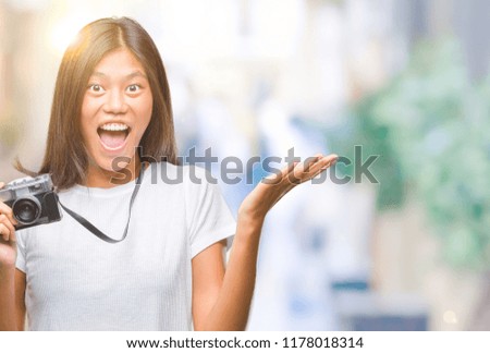 Young asian woman holding vintagera photo camera over isolated background very happy and excited, winner expression celebrating victory screaming with big smile and raised hands