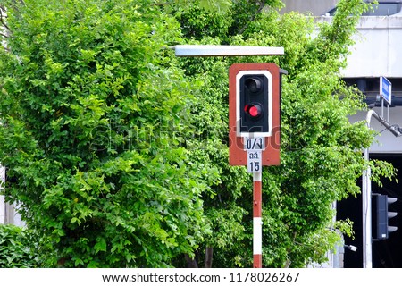A red light on the train sign pole at the railway station area with green nature background in Bangkok, Thailand (Thai alphabet on the sign means: Kho-khai/Ngo-ngu,Loling,SoSuea.15)