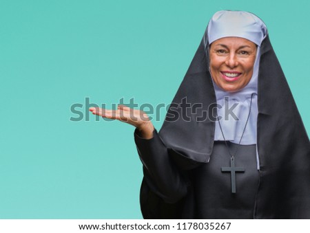 Middle age senior christian catholic nun woman over isolated background smiling cheerful presenting and pointing with palm of hand looking at the camera.