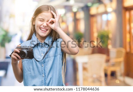 Young beautiful girl taking photos using vintage camera over isolated background with happy face smiling doing ok sign with hand on eye looking through fingers