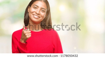 Young beautiful arab woman wearing winter sweater over isolated background doing happy thumbs up gesture with hand. Approving expression looking at the camera with showing success.