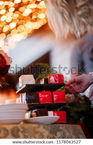 Wedding cake with red, white and brown squares. Wedding cake with bouquet on a blurry background placed on a table in a restaurant. The bride takes a piece of cake.