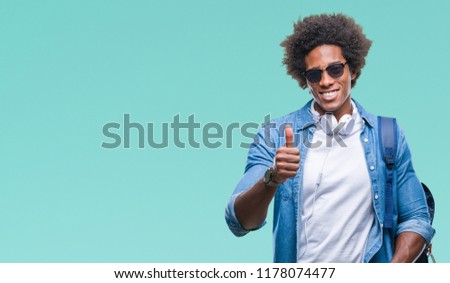 Afro american man wearing headphones and backpack over isolated background happy with big smile doing ok sign, thumb up with fingers, excellent sign