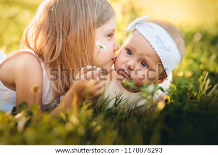 little girls 5 years old and baby lying on the grass, kisses on the cheek little sister