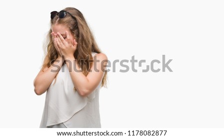 Young blonde woman wearing sunglasses with sad expression covering face with hands while crying. Depression concept.