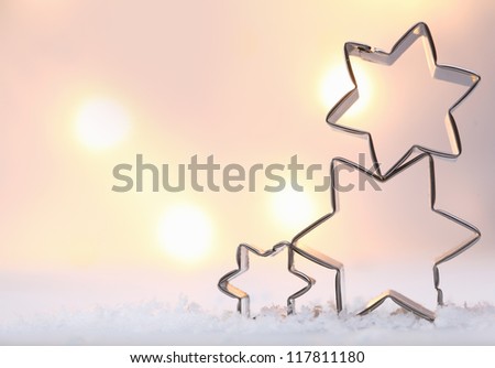 Atmospheric Christmas star background with three metal star cookie cutters balanced on top of each other on snow against a soft moody bokeh of glowing lights with copyspace