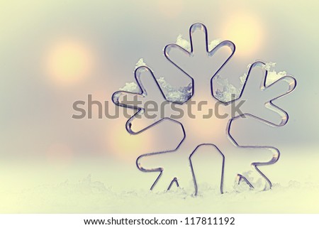 Ethereal snowflake Seasonal background with a snowflake-shaped metal cookie cutter oulined against soft muted Christmas lights with copysapce