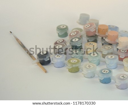 Watercolor paints, numbered, for drawing pictures by numbers and a paintbrush for drawing. A close-up shot on a white background.
