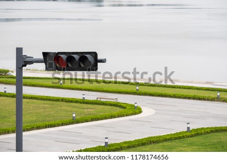Red traffic light at a crossroads by a lake with grass in the foreground