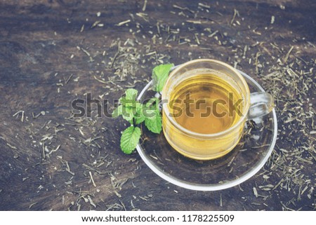Cup of hot tea and mint herb on wood background .