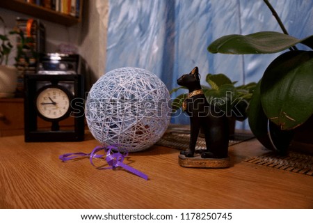 Cat figurine, thread ball and clock standing on the table in the house.
