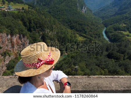 A young woman in a white blouse and straw hat watches the mountain river flowing among the stone gorge.