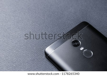 Black smartphone on a black textured surface is the back side.