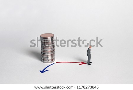 A miniature man standing before a red arrow in two directions with a pile of coins.