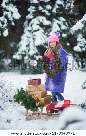 Portrait of girl in winter forest. Girl carries a Christmas tree and presents with sled. The concept of Christmas celebration Child waiting for a Christmas in the wood. Selective focus