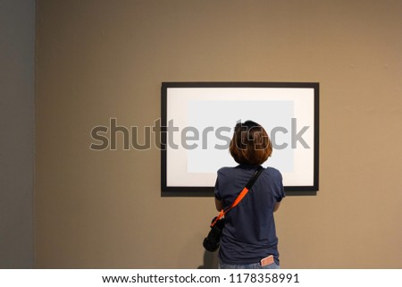 Woman is looking at blank photo frame on wall in art gallery.