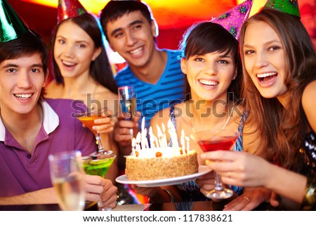 Portrait of joyful friends toasting and looking at camera at birthday party
