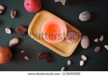 A nice picture with bright orange candle in the middle from the top view. Beautiful background with a few small stones and a couple of apples. 