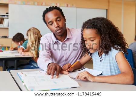 Teacher working with elementary school girl at her desk Royalty-Free Stock Photo #1178415445