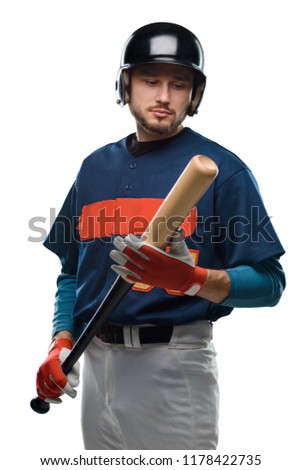Baseball player looking at a wooden bat in his hands. Bearded man dressed in a hitter gear, isolated on white.