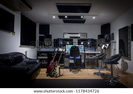 Recording studio control room complete with mixing desk, computer and outboard equipment. Also in the image are guitars, keyboard, microphone and synthesisers. Royalty-Free Stock Photo #1178434726