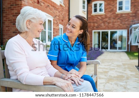 Senior Woman Sitting On Bench And Talking With Nurse In Retirement Home Royalty-Free Stock Photo #1178447566