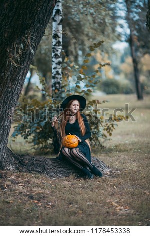 Beautiful modern witch with long red hair having fun in the autumn forest. Fashion Halloween concept